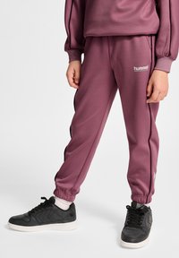 Maroon sweatpants med sorte sidestriber, ribbede manchetter og Hummel-logo. Parret med sorte sneakers med en struktureret overflade.