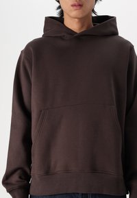 Brown hooded sweatshirt with a front pocket, long sleeves, and ribbed cuffs. Made of soft fabric with a smooth texture and minimal design.