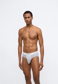 Sivé bavlnené nohavičky s bielym elastickým pásom pre značku Calvin Klein. Hladký povrch, priliehavý strih, stredne vysoký štýl.