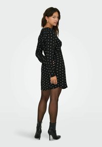Mustmustriibuline must kleit pikade varrukatega, valgete täppidega, keha vormiv, üle põlve pikkuses, koos mustade kontsadega ankle-boot'idega.