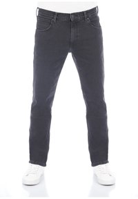 Černé denimové džíny s úzkým střihem, pěti kapsami a zapínáním na knoflík, doplněné bílými teniskami na jednobarevném pozadí.