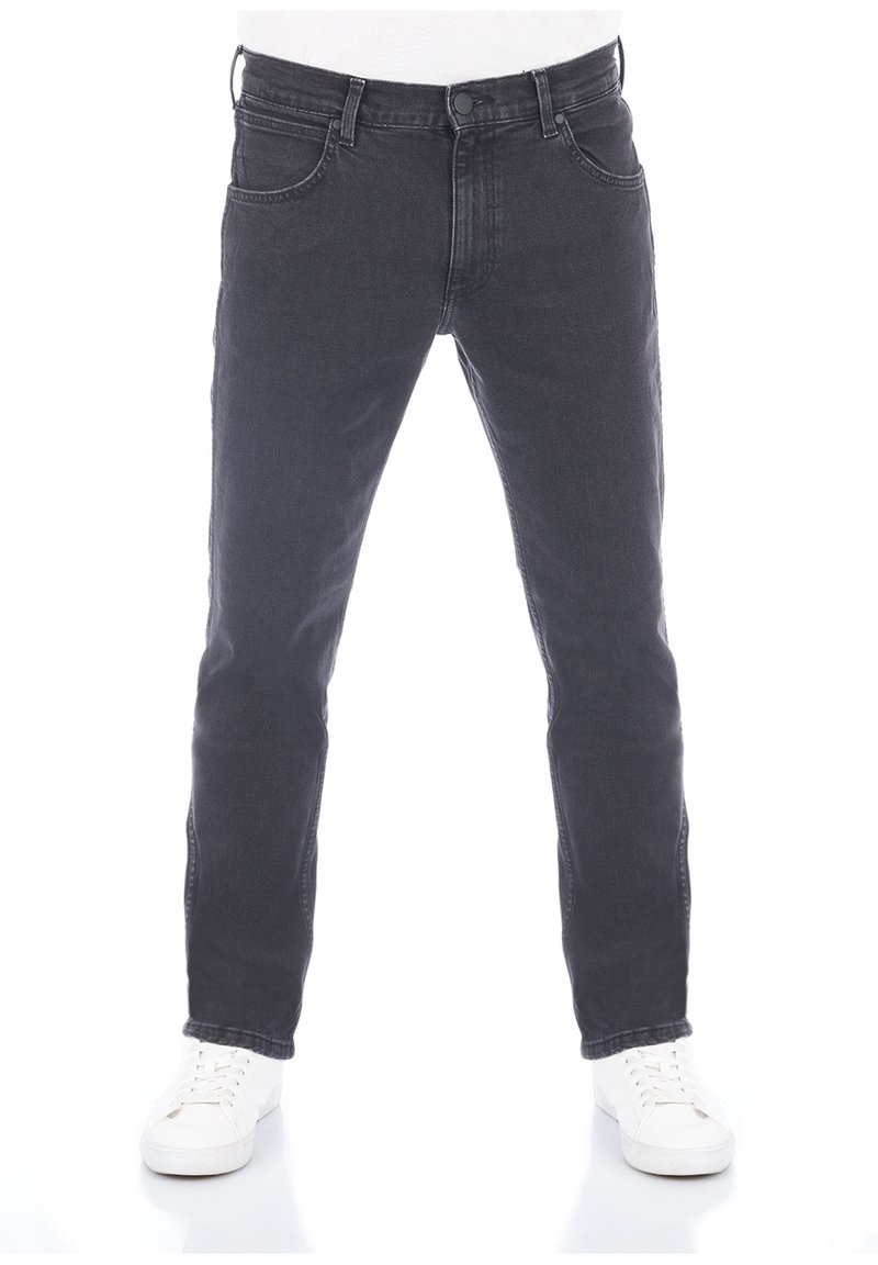 Svarta jeans i denim med smal passform, femficksdesign och knappstängning, kombinerade med vita sneakers mot en enfärgad bakgrund.