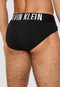 Zwarte katoenen boxershorts met een witte "Calvin Klein" logo op de elastische tailleband, met een zachte textuur en een stevige pasvorm.