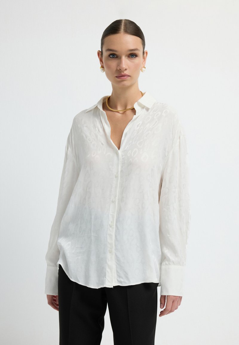 White button-up shirt with a subtle animal print pattern, long sleeves, and a relaxed fit, paired with black pants. Smooth, light fabric.