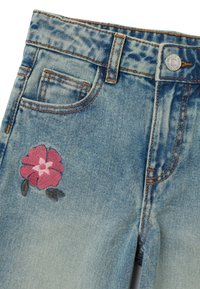 Jeans de mezclilla azul claro con un efecto deslavado, que presentan una flor bordada en rosa en el bolsillo delantero izquierdo y detalles de costura estándar.