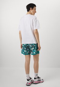 Hvid bomulds t-shirt, turkise shorts med et hvidt abstrakt mønster, sorte og hvide sneakers og hvide ankelstrømper.