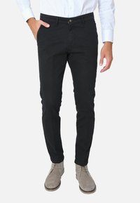 Chino neri con vestibilità slim, realizzati in cotone, con chiusura a bottone, tasche laterali e una texture liscia, abbinati a stivali in suede grigi.