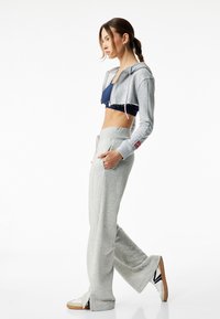 Szara skrócona bluza z kapturem z granatowym sportowym biustonoszem, w połączeniu z jasnoszarymi dresami. Materiał: dzianina bawełniana. Ciekawe detale: kieszenie i boczne rozcięcia.