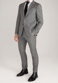 Traje gris a cuadros con diseño de corte slim, chaqueta de dos botones, solapas con muesca, pantalones a juego y botines de cuero negro.