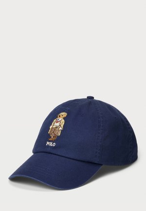 Marineblå bomullslue med en brodert bjørn i formell bekledning og "POLO"-tekst. Designet med en buet skjerm og justerbar stropp.