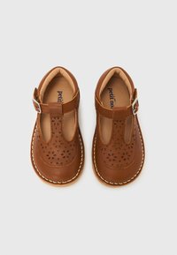 Καφέ δερμάτινα σανδάλια για νήπια με λουλουδάτο σχέδιο κοπής, μαξιλαρομένα πέλματα και ασημένιες αγκράφες σε λευκό φόντο.