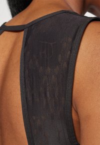 Top negro sin mangas con un panel trasero texturizado, que presenta un patrón sutil y un escote suave. La tela parece ligera y transpirable.