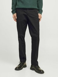 Sorte bukser med lige snit, lavet af glat stof. Båret med en grøn sweater og sorte snørebåndssko. Simpelt design, uden synlige mønstre.