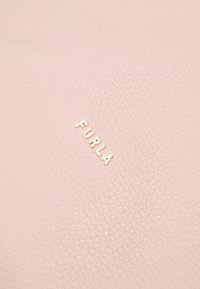 Vaaleanpunainen nahkamateriaali, jossa on teksturoitu pinta ja kultainen "Furla"-logo. Muotoilu on yksinkertainen ja nykyaikainen.