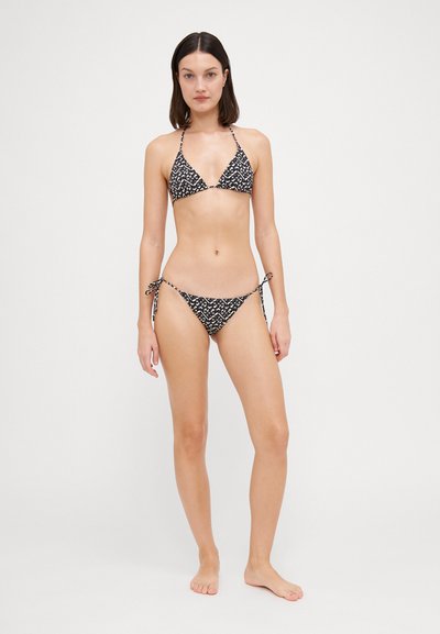 Melnām un baltām svītrām izstrādāta trīsstūru bikini komplekts ar saitēm sānos. Materiāls izskatās gluds; ar plānām siksnām un minimālu segumu.