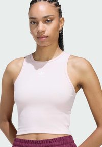 Svetloružový skrátený top s rebrovanou textúrou, s okrúhlym výstrihom a bielym logom Adidas, skombinovaný s tmavofialovými šortkami s elastickým pásom.