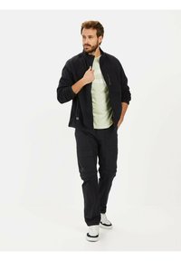 Sort fleecejakke med en lynlåslomme, parret med sorte cargo-bukser med flere lommer og hvide sneakers. Lys grøn skjorte nedenunder.