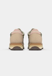 Saucony sneakers featuring a light beige upper, green accents, pink heel collar, and a layered white and brown sole with textured grips.