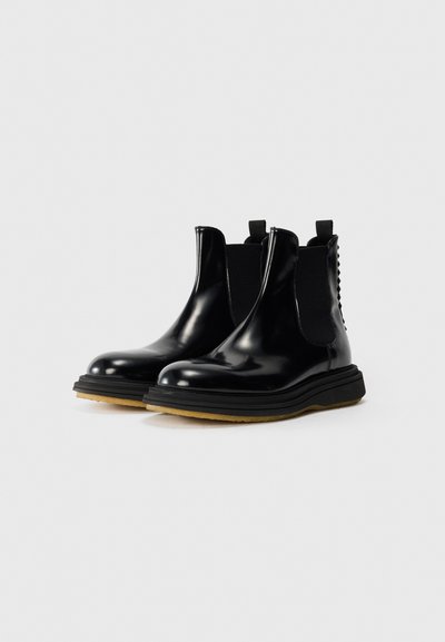 Botas Chelsea negras y brillantes con paneles laterales elásticos, punteras redondeadas, suela gruesa negra y suela de goma contrastante para mayor tracción.