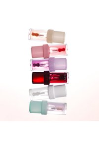 Glosses à lèvres Nabla dans des tubes en plastique transparent, présentant une gamme de couleurs : rouge, rose, violet et menthe. Chaque bouchon est doté d'une bande texturée.