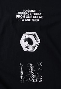 Μαύρο ύφασμα με λευκό κείμενο: "ΠΑΡΑΠΕΡΝΩ ΑΝΕΠΑΙΣΘΗΤΑ ΑΠΟ ΜΙΑ ΣΚΗΝΗ ΣΕ ΑΛΛΗ." Από κάτω, ένα γραφικό με εξαγωνικό παξιμάδι και αφηρημένο σχέδιο.