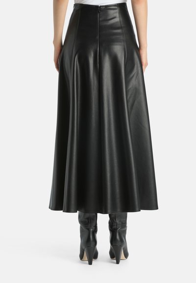 Schwarze Leder-Maxikleid mit glatter Oberfläche, hoher Taille und fließendem Schnitt. Reißverschluss auf der Rückseite. Kombiniert mit kniehohen schwarzen Stiefeln mit Absatz.
