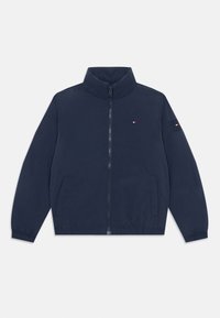 Veste légère bleu marine avec un col haut, fermeture éclair à l'avant et deux poches latérales. Présente des poignets élastiques et un petit logo sur la poitrine.