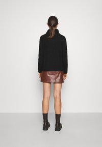 Svart, strukturerad tröja med hög hals, kombinerad med en brun, glansig läderminikjol. Svarta ankelstövlar kompletterar outfiten.