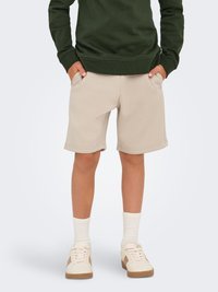 Beige bomuldsshorts med sidelommer, parret med hvide strukturerede sokker og lyse sneakers. Overdelen er en mørkegrøn sweatshirt.