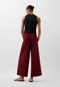 Černý žebrovaný top bez rukávů v kombinaci s širokými maroon kalhotami s zadními kapsami, na světlém pozadí. Černé sandály na pásky.