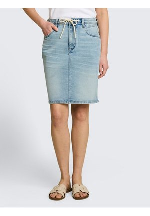 Frau trägt einen hellblauen Jeansrock mit Fronttaschen und Kordelzug in der Taille, kombiniert mit beigen Slip-On-Sandalen und einem weißen Oberteil.