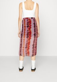 Femme portant une jupe midi rayée violet et rouge, un débardeur blanc, des chaussettes blanches et des baskets noires à tige basse, vue de dos.
