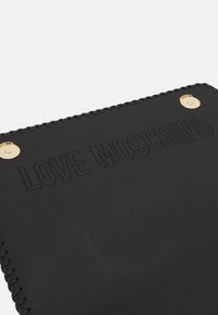 Černý syntetický kožený zápisník s embosovaným textem "LOVE MOSCHINO". Obsahuje zlaté kovové prvky a dekorativní prošívání podél okraje.