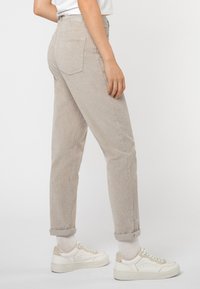 Beige corduroy broek met een tapered fit, omgeslagen pijpen en twee achterzakken, gecombineerd met witte sneakers met beige accenten.