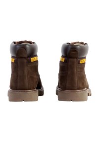 Stivali alla caviglia in suede marrone con accenti in pelle marrone scuro, punta rotonda, collo imbottito e logo giallo "Caterpillar" nella parte posteriore.