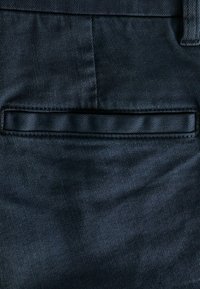 Tejido de mezclilla azul oscuro con un bolsillo trasero visible de diseño plano y textura suave. Bordes cosidos con hilo a juego.
