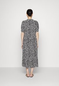 Vestido midi em padrão de zebra preto e branco com mangas bufantes, cintura ajustada e saia em camadas, feito de tecido leve. Sandálias rasas usadas.