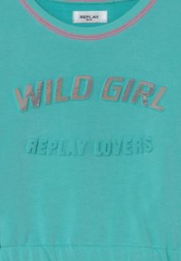 Vestido de algodão turquesa com texto prateado em relevo, brilhante, "WILD GIRL" e "REPLAY LOVERS" em relevo na parte da frente. Design simples e casual.