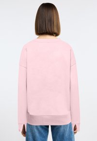 Roze sweater met een ontspannen pasvorm, lange mouwen en een gebogen zoom. Het materiaal lijkt zacht met een gladde textuur. Heeft zijsplitten.