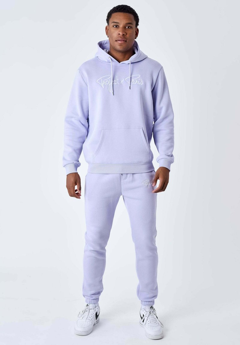 Sweat à capuche lilas et joggings assortis, tous deux en tissu doux. Le sweat à capuche possède une poche avant et un logo blanc ; les joggings ont des poignets élastiques et un cordon de serrage.