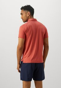 Kortermet polo skjorte i korall med en teksturert overflate, sidesplitt, båret med mørk marineblå shorts, som viser en tettsittende design.