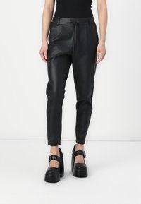 Zwarte nep leren broek met een tapered fit, voorzien van een drawstring taille en een gladde textuur. Gepaarde met stevige zwarte platform schoenen.