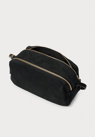 Borsa da toiletta rettangolare in suede nero con due cerniere dorate visibili, di cui una parzialmente aperta, e un piccolo manico ad anello su un'estremità.