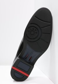 Suola di scarpa nera con gomma testurizzata, marchio circolare, un accento blu e una striscia rossa. Presenta un battistrada scanalato per una migliore aderenza.