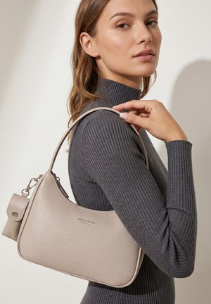 Donna con dolcevita grigio a coste che porta una borsa beige Diana & Co Firenze sulla spalla su uno sfondo neutro.