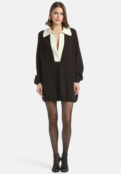 Preližité tmavohnedé šaty s hlbokým V-výstrihom a krémovým golierom. Dlhé rukávy a elastický lem. Nosené s priesvitnými čiernymi pančuchami.