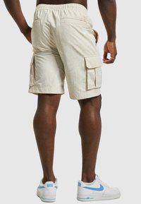 Beige cargo shorts med elastisk midje, to side lommer og to baklommer. Laget av lett stoff, med en teksturert overflate.