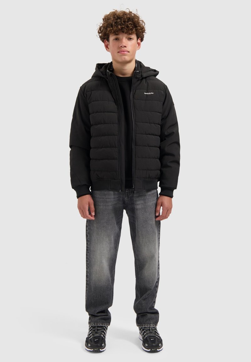 Zwart donzen jack met capuchon, voorzien van doorgestikte delen. Gecombineerd met donkergrijze jeans en zwarte sneakers, effen achtergrond.