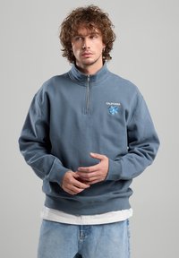 Blue cotton sweatshirt with half-zip collar, embroidered "CALIFORNIA" text, and floral design. Features ribbed cuffs and hem.