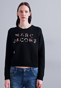 Black knitted sweater with a cropped design, featuring multicolored, textured lettering spelling "MARC JACOBS" on the front.